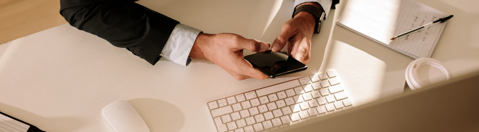 Man typing on cell phone in front of computer
